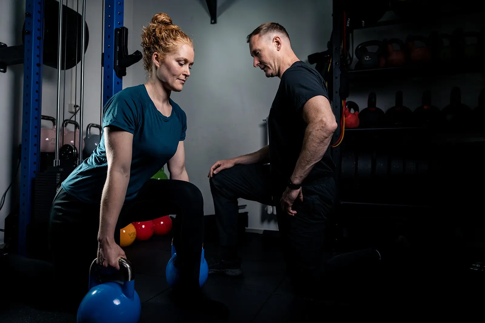Frau hebt zwei Kettlebells, Trainer beobachtet die Ausführung