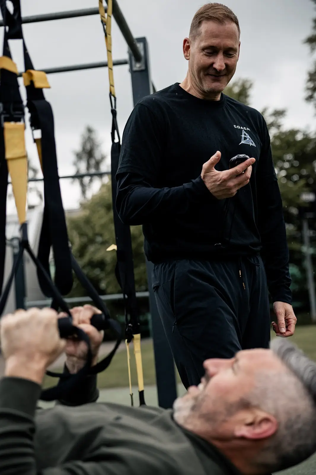 Trainer betreut einen Mann beim Schlingentraining im Freien